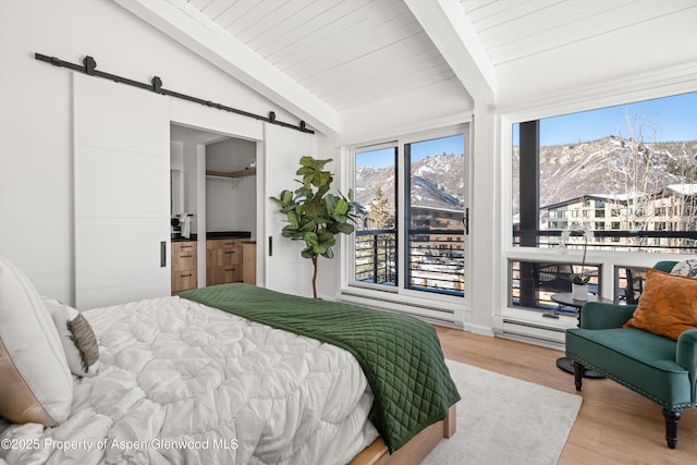 bedroom with a barn door, lofted ceiling with beams, a baseboard radiator, a mountain view, and light hardwood / wood-style floors