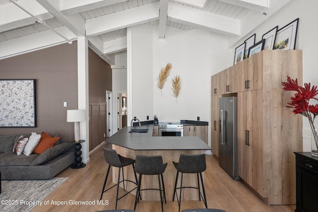 kitchen featuring sink, vaulted ceiling with beams, light hardwood / wood-style floors, a breakfast bar area, and appliances with stainless steel finishes