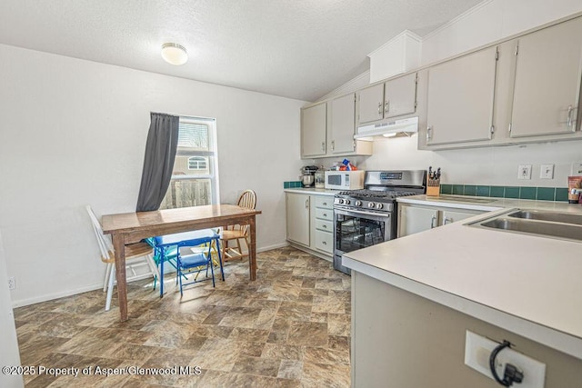 kitchen with lofted ceiling, stone finish floor, under cabinet range hood, stainless steel gas stove, and white microwave