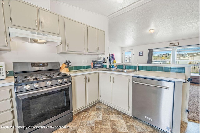 kitchen with under cabinet range hood, appliances with stainless steel finishes, light countertops, a sink, and a peninsula