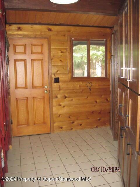 entrance foyer with wood walls, light tile patterned floors, and beamed ceiling