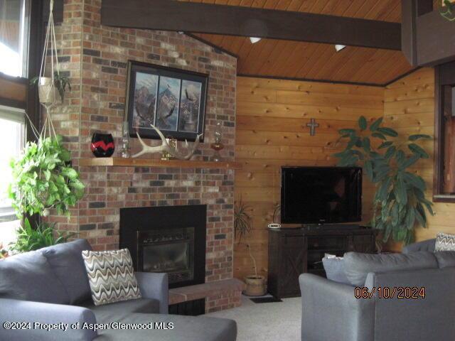 carpeted living area featuring lofted ceiling with beams, a brick fireplace, wood ceiling, and wooden walls