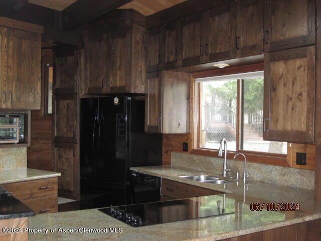 kitchen with black appliances, light stone counters, brown cabinetry, and a sink