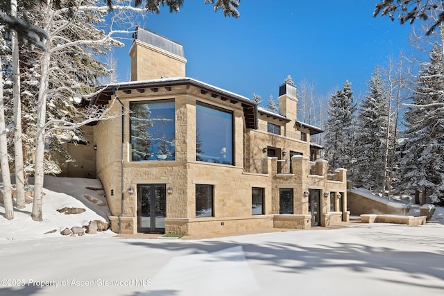 view of snow covered exterior with stone siding and a chimney