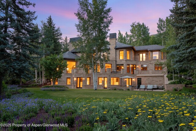 64 Pitkin Way, Aspen, CO 81611 - back of property at dusk featuring a chimney, an outdoor hangout area, a balcony, a yard, and a patio