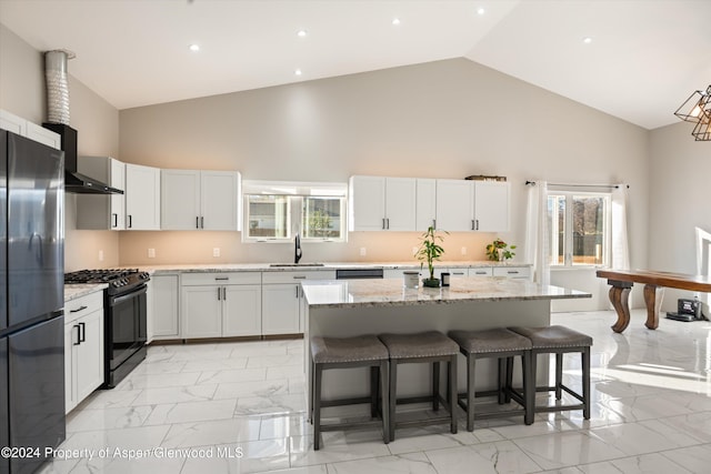 kitchen featuring a center island, gas stove, light stone countertops, and stainless steel refrigerator