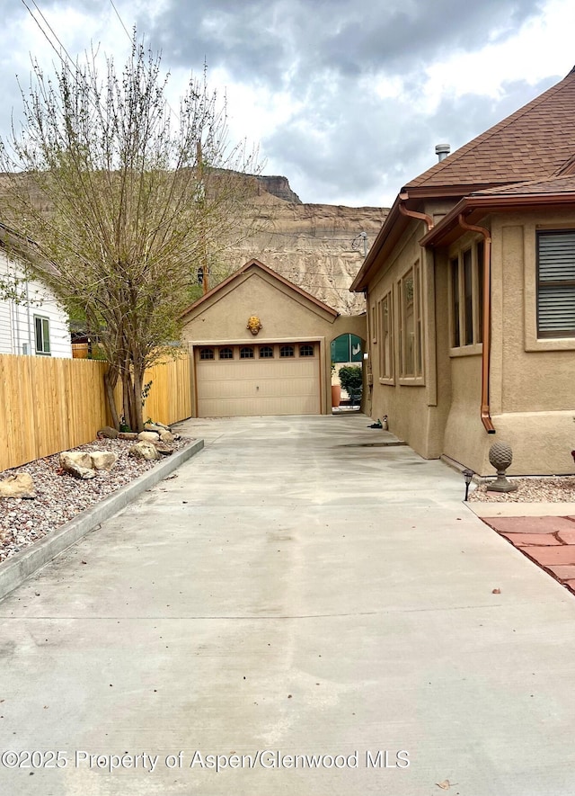 view of home's exterior featuring fence, stucco siding, driveway, an outdoor structure, and a garage