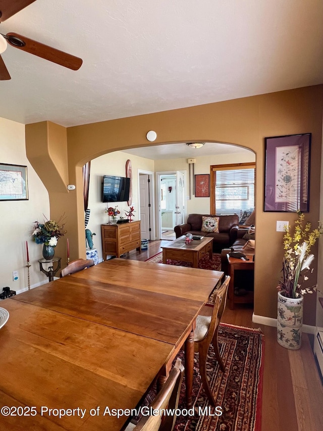 dining room featuring a baseboard heating unit, arched walkways, baseboards, wood finished floors, and ceiling fan