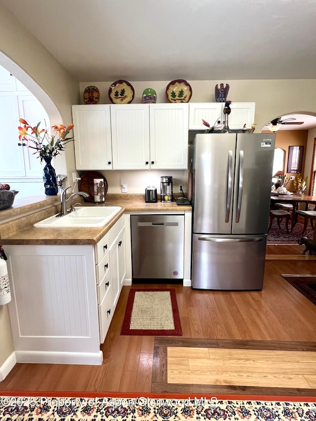 kitchen with white cabinets, arched walkways, a sink, appliances with stainless steel finishes, and wood-type flooring