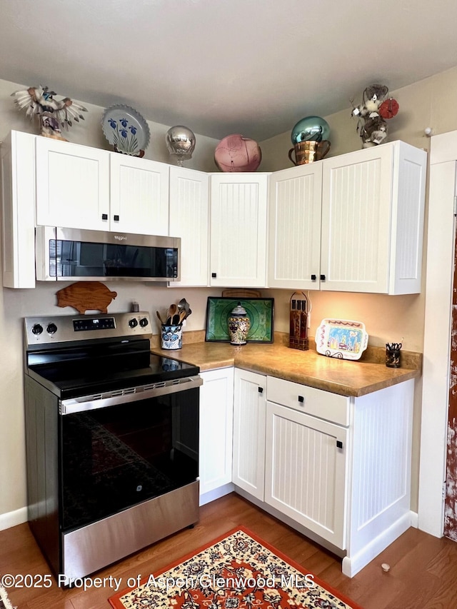 kitchen with light wood-style flooring, baseboards, white cabinetry, and appliances with stainless steel finishes