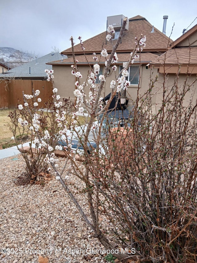 exterior space featuring stucco siding, roof with shingles, and fence