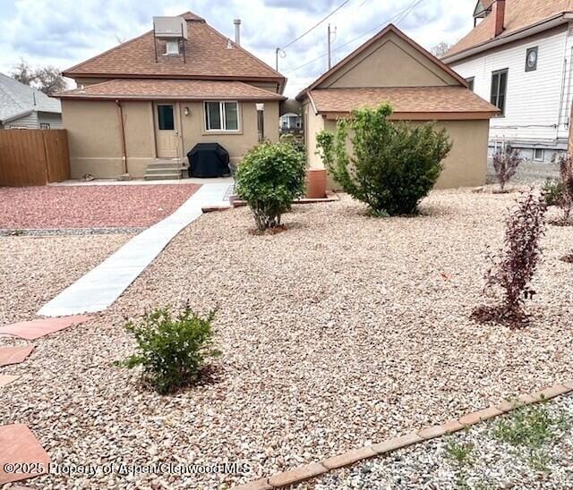 back of property with fence, a shingled roof, entry steps, and stucco siding