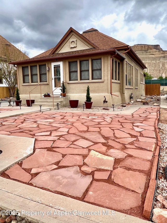 back of house with roof with shingles, a patio, stucco siding, and fence
