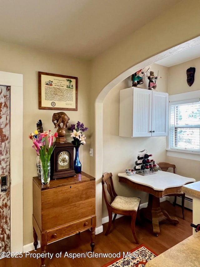 dining space featuring baseboards, wood finished floors, and arched walkways