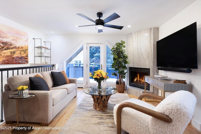 living room with baseboard heating, ceiling fan, a fireplace, and light hardwood / wood-style flooring