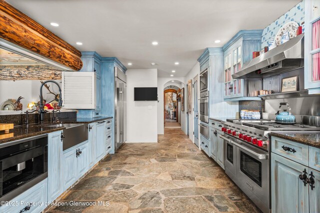87 Magnifico Dr, Aspen, CO 81611 - kitchen with appliances with stainless steel finishes, arched walkways, light stone finish flooring, dark stone countertops, and a warming drawer