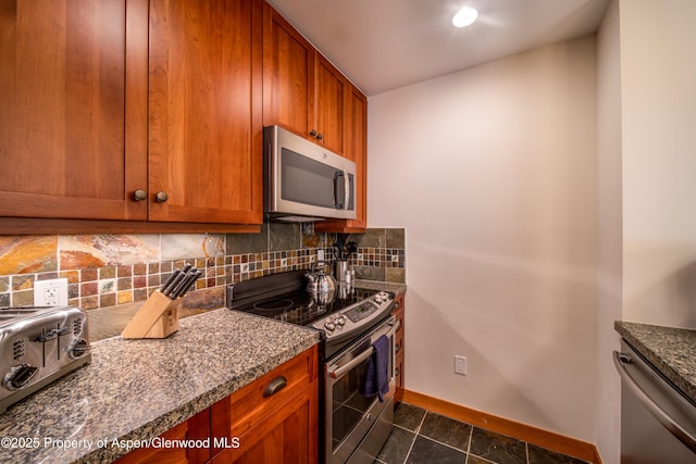 kitchen with stone countertops, stainless steel appliances, baseboards, backsplash, and brown cabinets