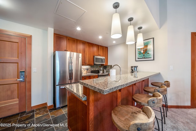 kitchen featuring decorative light fixtures, stainless steel appliances, tasteful backsplash, brown cabinetry, and a peninsula