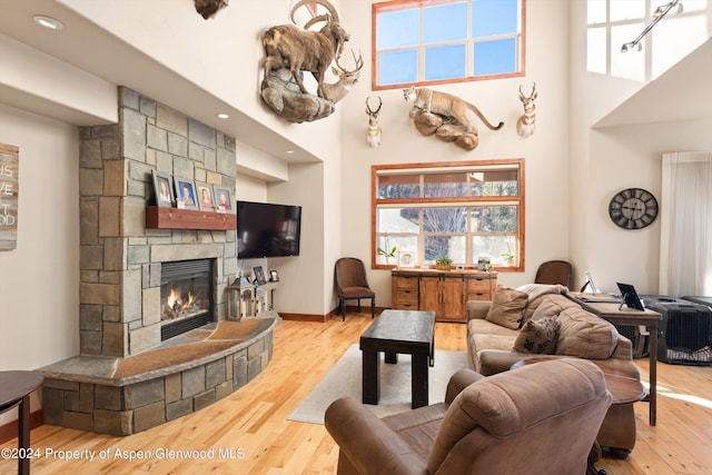 living room featuring a stone fireplace, wood-type flooring, and a high ceiling