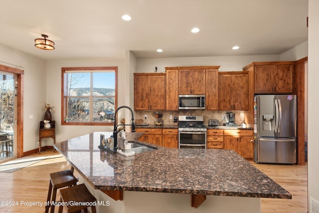 kitchen featuring sink, appliances with stainless steel finishes, tasteful backsplash, an island with sink, and a kitchen bar