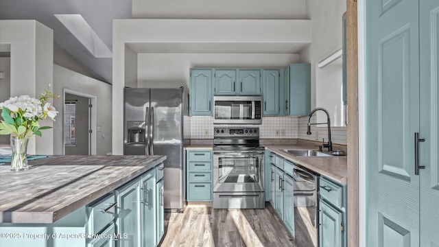 kitchen featuring decorative backsplash, appliances with stainless steel finishes, a sink, blue cabinets, and light wood-type flooring