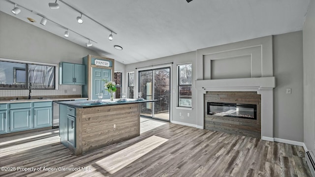 kitchen featuring blue cabinets, a sink, wood finished floors, tasteful backsplash, and a glass covered fireplace