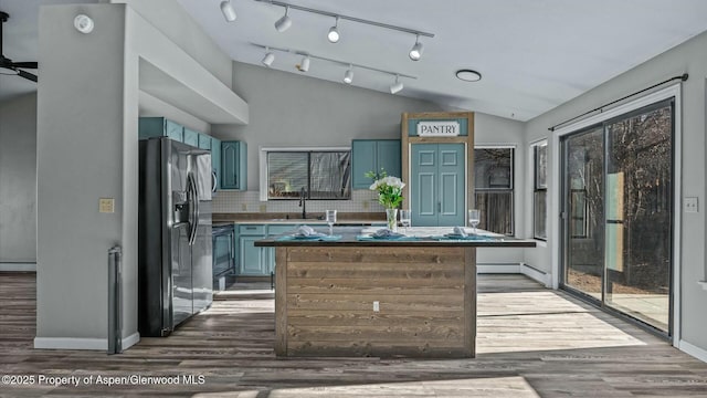 kitchen with vaulted ceiling, blue cabinetry, a sink, and stainless steel fridge with ice dispenser