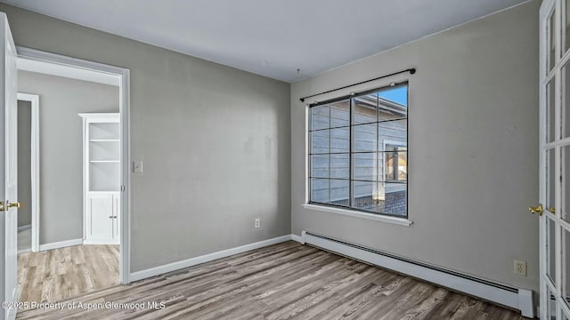 empty room with baseboard heating, wood finished floors, and baseboards