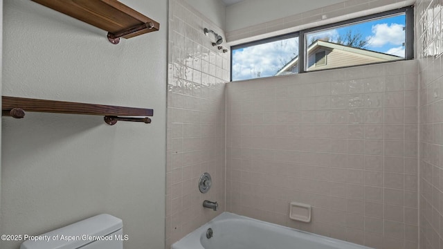 bathroom featuring a textured wall, shower / bathing tub combination, and toilet