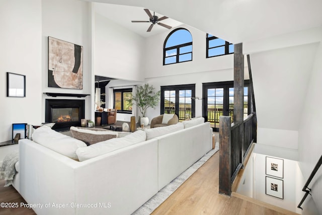 living room featuring a glass covered fireplace, ceiling fan, light wood finished floors, a high ceiling, and french doors