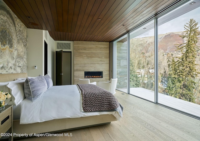 bedroom with a mountain view, wooden ceiling, expansive windows, access to exterior, and a large fireplace