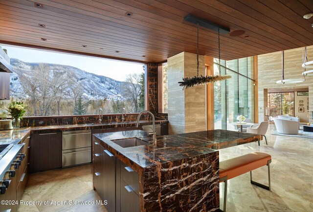 kitchen featuring a mountain view, sink, dark stone countertops, dark brown cabinetry, and wood ceiling