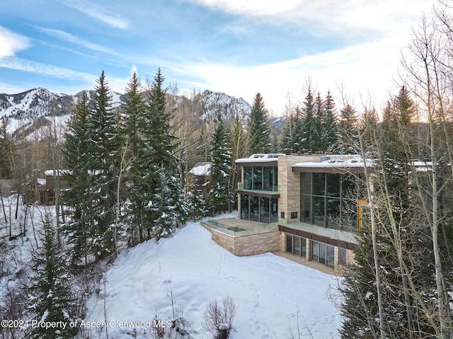 snow covered back of property with a sunroom, a mountain view, and a hot tub