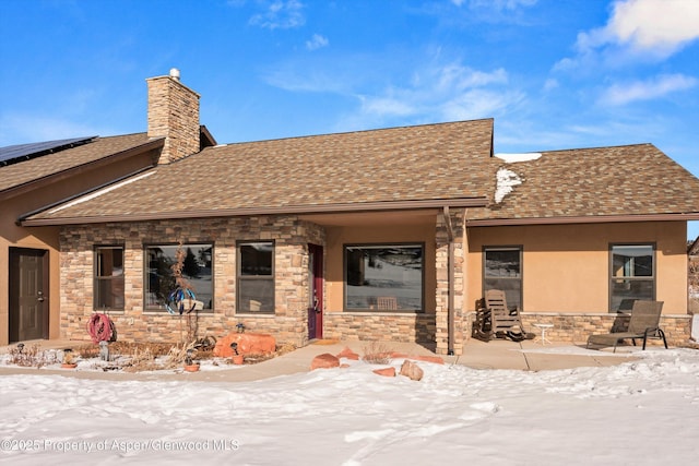 view of front of house featuring stone siding, roof with shingles, a chimney, and stucco siding