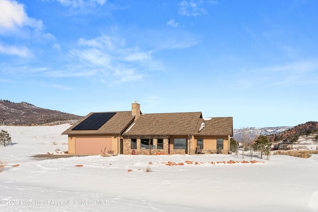 view of front of property with roof mounted solar panels, a mountain view, a chimney, and an attached garage