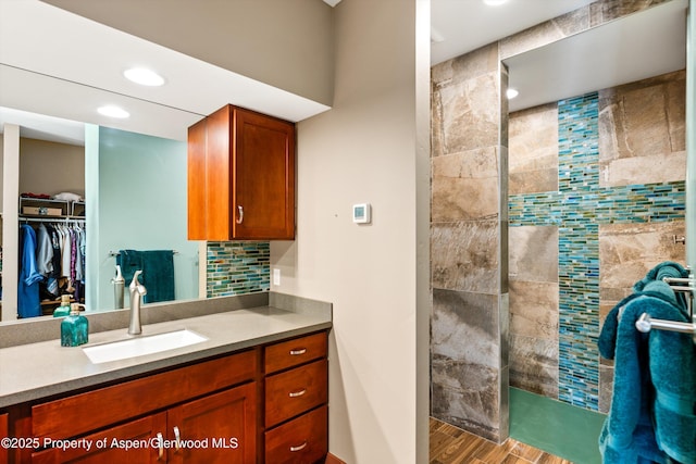 full bath featuring recessed lighting, a spacious closet, vanity, wood finished floors, and a walk in shower