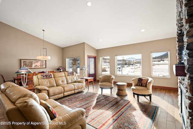 living room featuring baseboards, lofted ceiling, light wood-style flooring, a stone fireplace, and recessed lighting