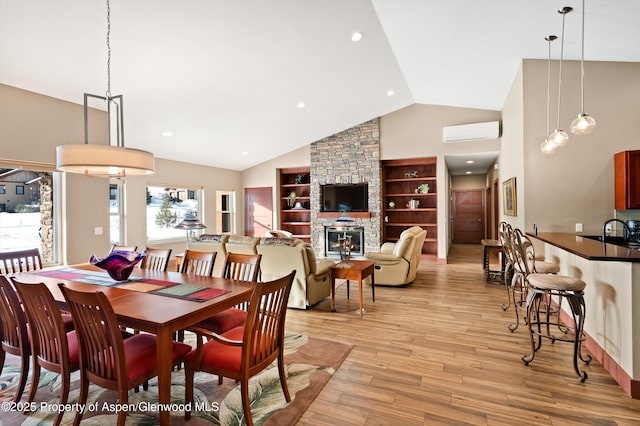 dining space featuring a wall unit AC, a stone fireplace, light wood-style floors, built in shelves, and high vaulted ceiling