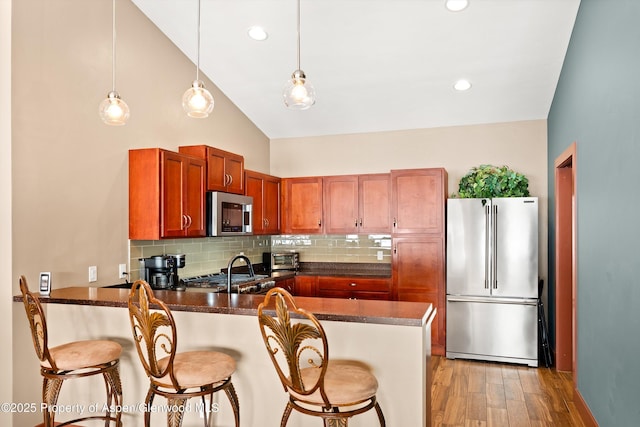 kitchen with light wood finished floors, decorative backsplash, a peninsula, stainless steel appliances, and a kitchen bar