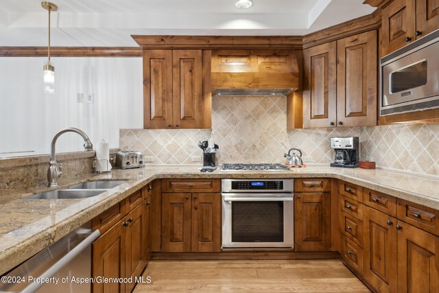 kitchen with appliances with stainless steel finishes, decorative light fixtures, sink, backsplash, and light wood-type flooring