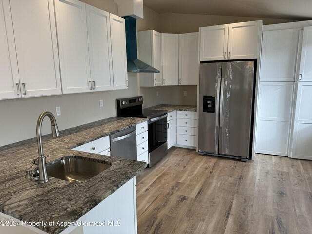 kitchen with wall chimney range hood, sink, appliances with stainless steel finishes, white cabinetry, and dark stone counters