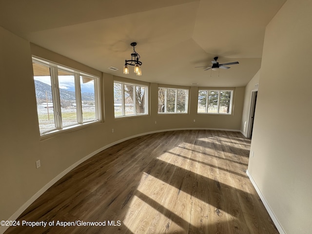 empty room with wood-type flooring, lofted ceiling, a healthy amount of sunlight, and a chandelier