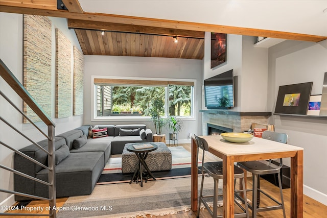 living room with a warm lit fireplace, a wealth of natural light, and vaulted ceiling with beams