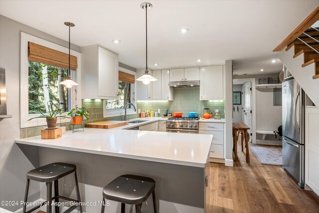 kitchen with wood finished floors, decorative light fixtures, a peninsula, stainless steel appliances, and light countertops