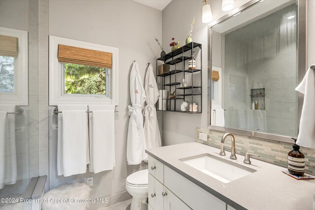 bathroom featuring toilet, tiled shower, vanity, and tasteful backsplash