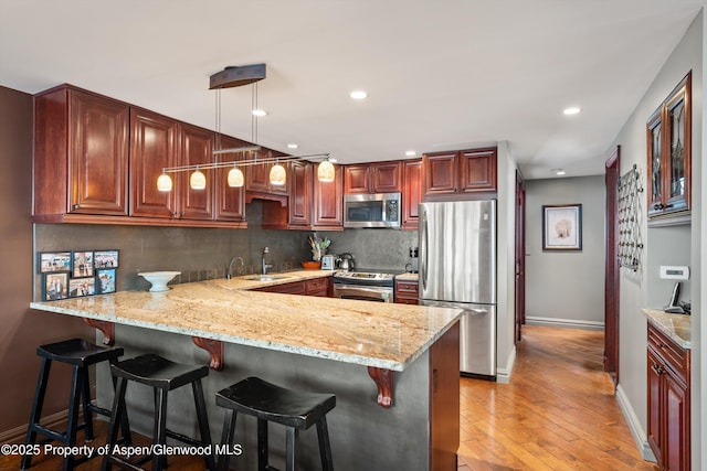 kitchen with appliances with stainless steel finishes, light stone counters, light wood finished floors, a peninsula, and backsplash