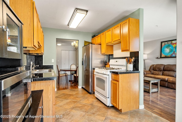 kitchen with a sink, white gas stove, a chandelier, decorative backsplash, and stainless steel fridge with ice dispenser