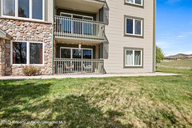 rear view of property featuring a lawn, stone siding, and a balcony