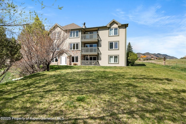 rear view of property with a lawn, stone siding, and a balcony