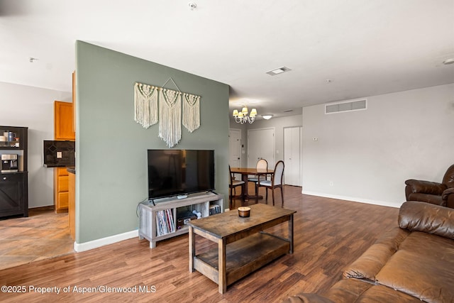 living room with baseboards, wood finished floors, visible vents, and an inviting chandelier